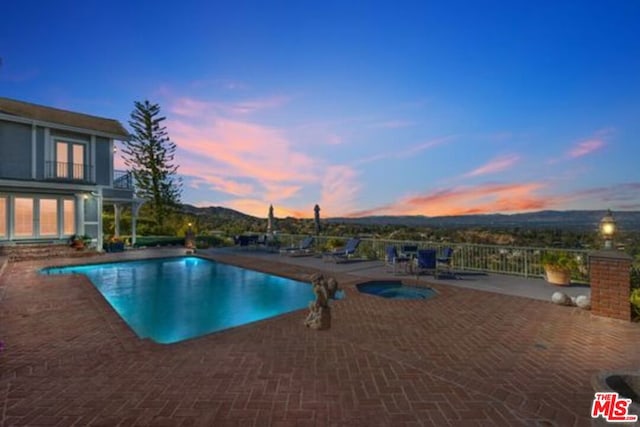 pool at dusk featuring a patio area, a mountain view, and an in ground hot tub