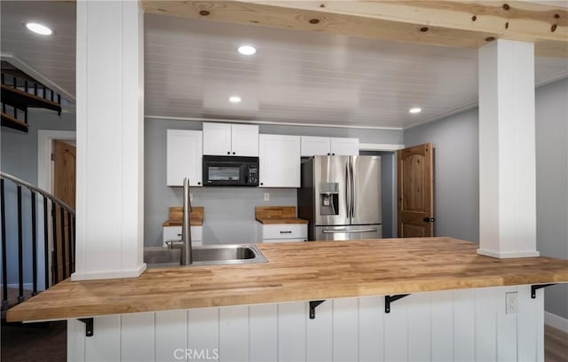 kitchen featuring a kitchen bar, stainless steel fridge, wooden counters, white cabinets, and sink