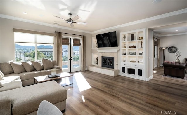 living room with wood-type flooring, ornamental molding, ceiling fan, a high end fireplace, and french doors