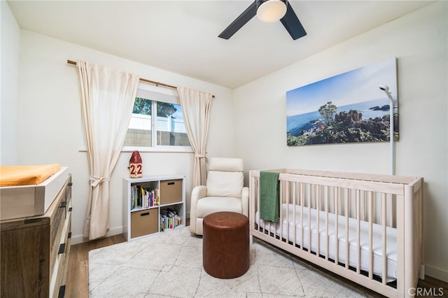 bedroom with ceiling fan, hardwood / wood-style floors, and a nursery area