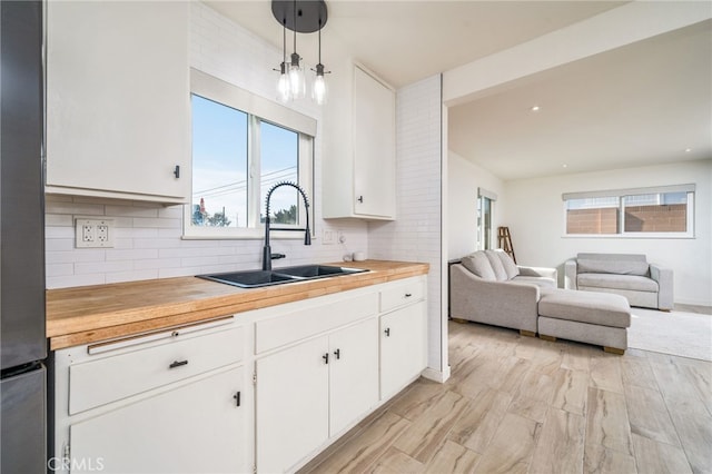 kitchen featuring pendant lighting, decorative backsplash, sink, white cabinetry, and wood counters