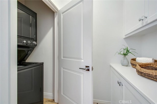 washroom featuring stacked washer / drying machine and cabinets