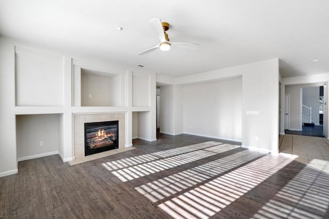 unfurnished living room featuring ceiling fan, built in features, wood-type flooring, and a tile fireplace