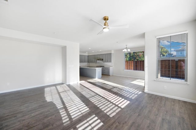 unfurnished living room with ceiling fan with notable chandelier and hardwood / wood-style flooring