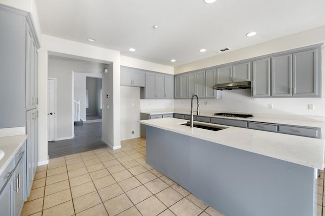 kitchen with stainless steel gas stovetop, light tile patterned floors, gray cabinetry, a kitchen island with sink, and sink