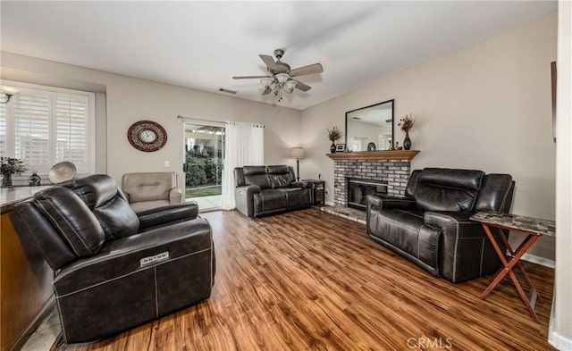 living room featuring ceiling fan, a healthy amount of sunlight, a brick fireplace, and hardwood / wood-style floors