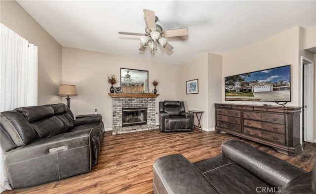 living room with a brick fireplace, wood-type flooring, and ceiling fan