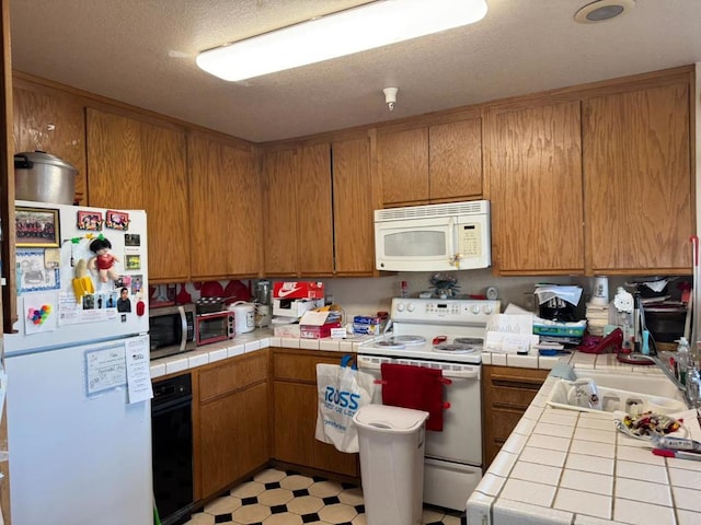 kitchen featuring white appliances, tile countertops, sink, and a textured ceiling