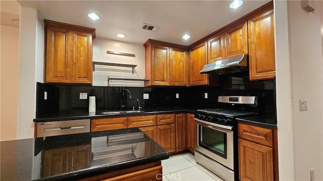 kitchen featuring light tile patterned floors, stainless steel appliances, decorative backsplash, dark stone countertops, and sink