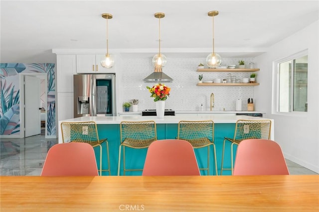 interior space featuring tasteful backsplash, stainless steel refrigerator with ice dispenser, sink, hanging light fixtures, and white cabinets