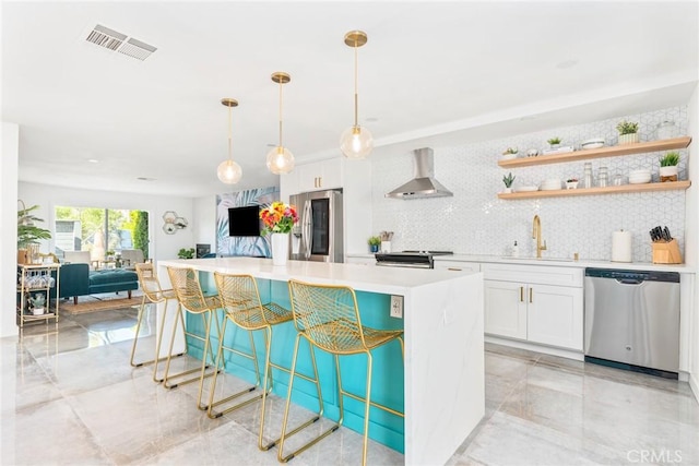 kitchen featuring decorative light fixtures, sink, appliances with stainless steel finishes, white cabinets, and wall chimney exhaust hood