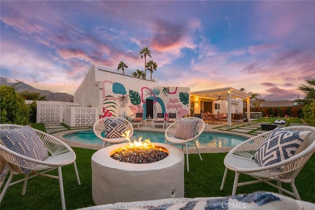 back house at dusk with a pergola, a patio area, and an outdoor fire pit