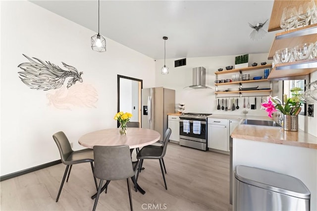 kitchen with wall chimney range hood, sink, white cabinetry, hanging light fixtures, and stainless steel appliances