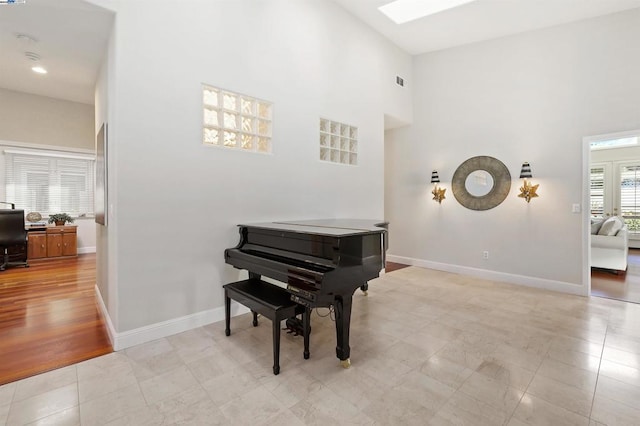 miscellaneous room with a towering ceiling, light tile patterned floors, and a skylight