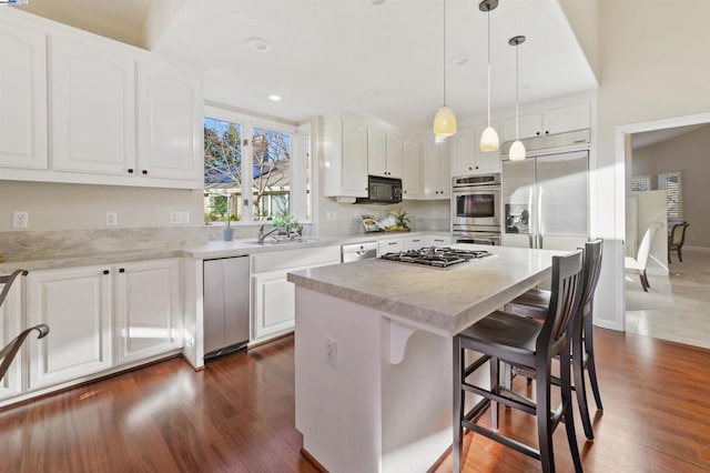 kitchen featuring white cabinetry, hanging light fixtures, a kitchen island, stainless steel appliances, and light stone countertops