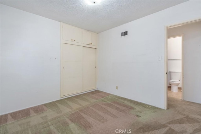 unfurnished bedroom with light colored carpet, a closet, and a textured ceiling