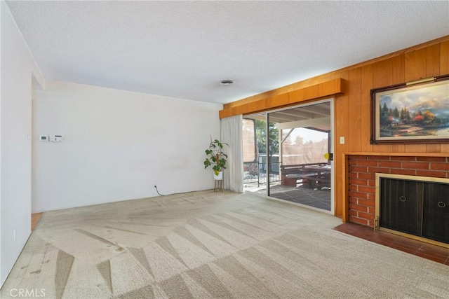 unfurnished living room with a brick fireplace, wood walls, a textured ceiling, and carpet flooring