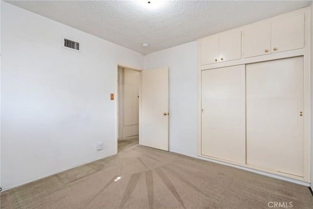 unfurnished bedroom with light colored carpet, a closet, and a textured ceiling