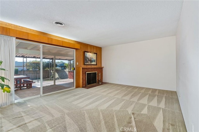 unfurnished living room featuring light colored carpet, a textured ceiling, wooden walls, and a fireplace