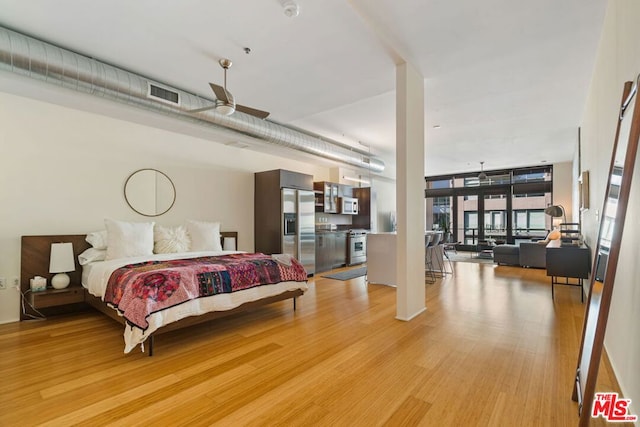 bedroom featuring light hardwood / wood-style floors, stainless steel fridge, and expansive windows