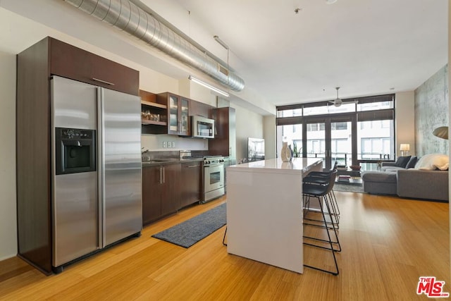 kitchen with appliances with stainless steel finishes, a kitchen island, a breakfast bar, light hardwood / wood-style flooring, and dark brown cabinets