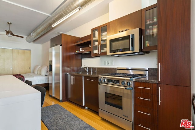 kitchen featuring stainless steel appliances, dark stone countertops, sink, ceiling fan, and light hardwood / wood-style flooring