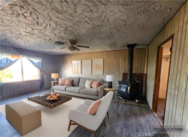 living room with ceiling fan, a wood stove, and wood walls