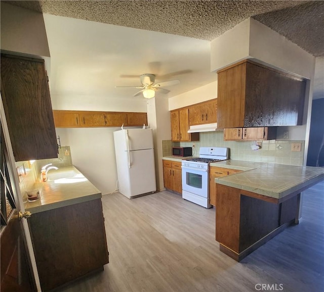 kitchen with tasteful backsplash, light hardwood / wood-style floors, kitchen peninsula, sink, and white appliances