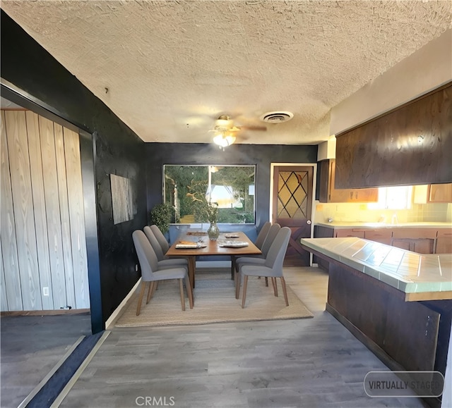 dining space with ceiling fan, a textured ceiling, and light hardwood / wood-style flooring