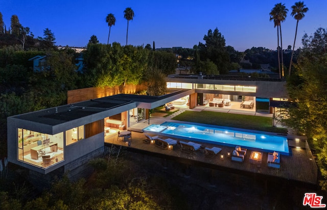 back house at dusk featuring a bar, an outdoor kitchen, outdoor lounge area, and a patio