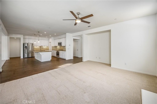 unfurnished living room featuring ceiling fan, sink, and dark colored carpet