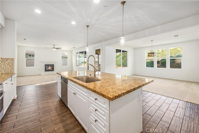 kitchen with decorative light fixtures, light stone countertops, sink, and a center island with sink