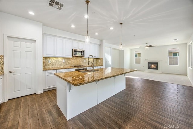 kitchen featuring sink, hanging light fixtures, stainless steel appliances, white cabinets, and a center island with sink