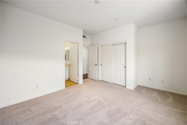 unfurnished bedroom with light carpet, ensuite bath, and a closet