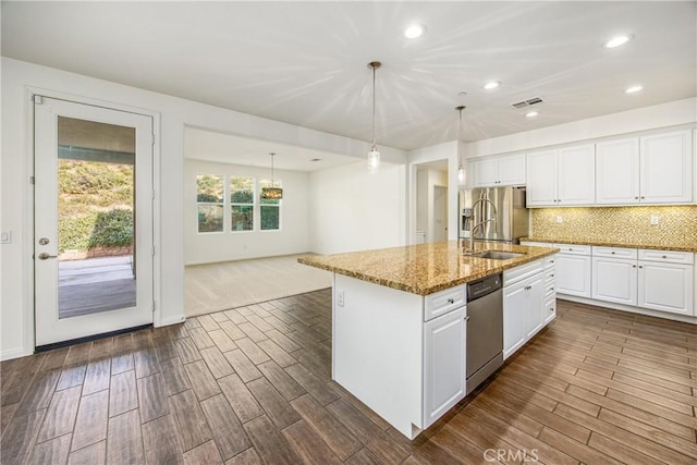 kitchen with white cabinetry, stainless steel appliances, light stone countertops, an island with sink, and decorative light fixtures