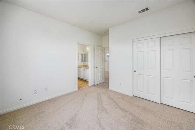 unfurnished bedroom with ensuite bath, light colored carpet, and a closet