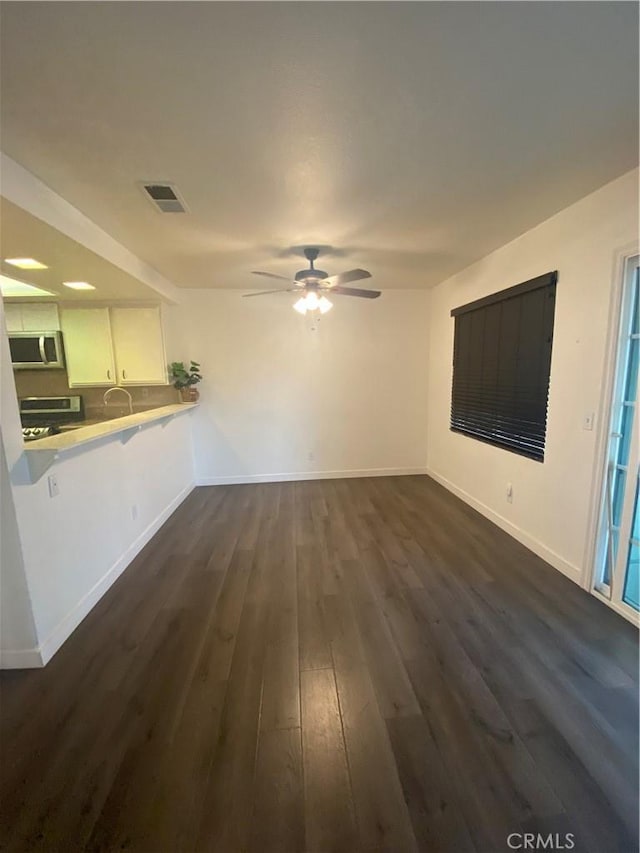 unfurnished living room featuring dark wood-type flooring and ceiling fan