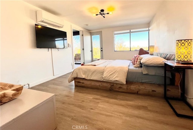 bedroom with a wall mounted AC, access to exterior, and hardwood / wood-style flooring