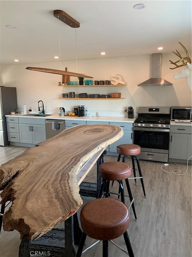 kitchen with appliances with stainless steel finishes, decorative light fixtures, light wood-type flooring, wall chimney range hood, and sink