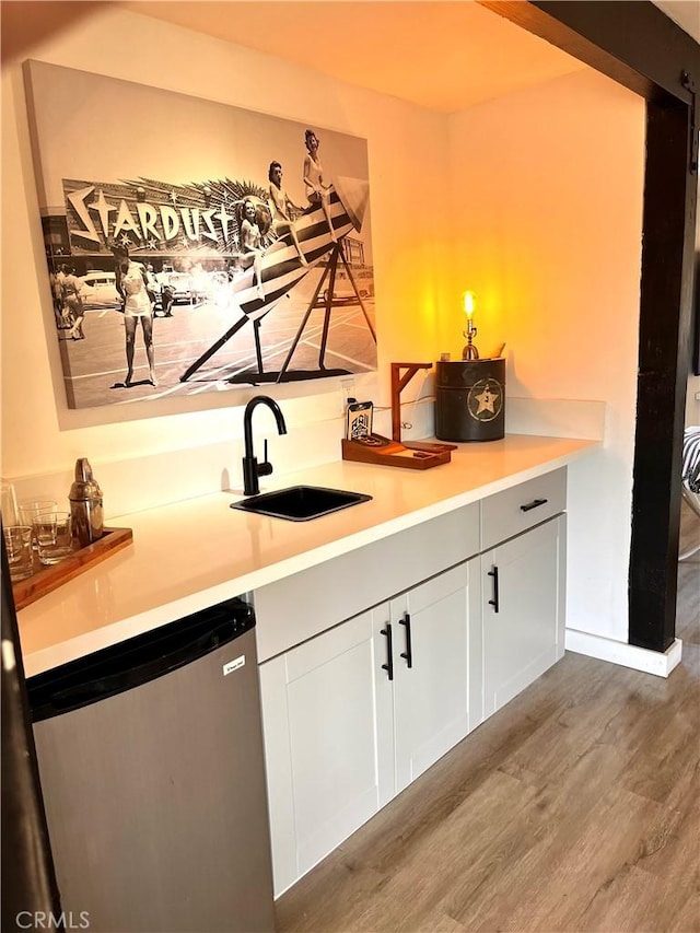 bar with sink, dishwashing machine, white cabinets, and hardwood / wood-style floors