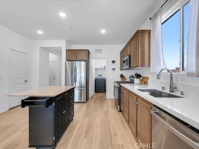 kitchen featuring a kitchen island, sink, light hardwood / wood-style flooring, appliances with stainless steel finishes, and a kitchen breakfast bar