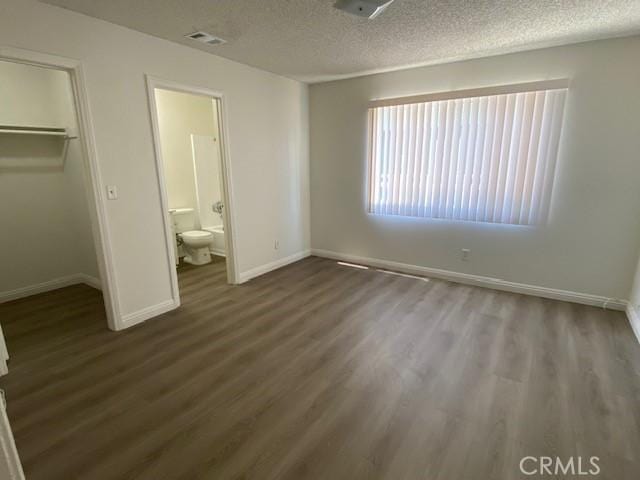 unfurnished bedroom with ensuite bathroom, dark hardwood / wood-style floors, a spacious closet, a textured ceiling, and a closet