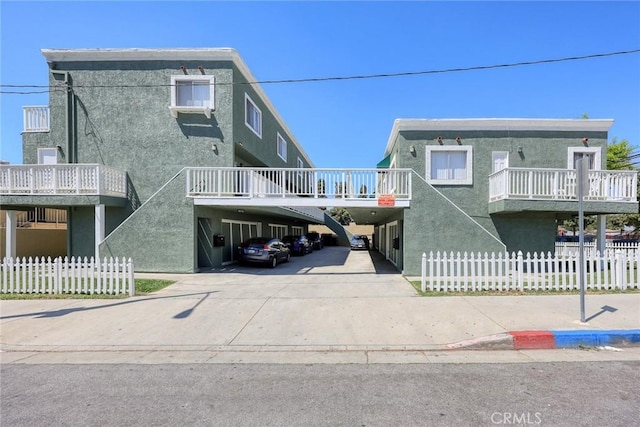 view of front of home featuring stairway, fence, concrete driveway, stucco siding, and a carport