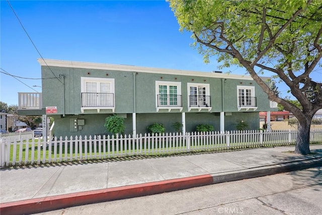 view of front of home with stucco siding, a balcony, and a fenced front yard