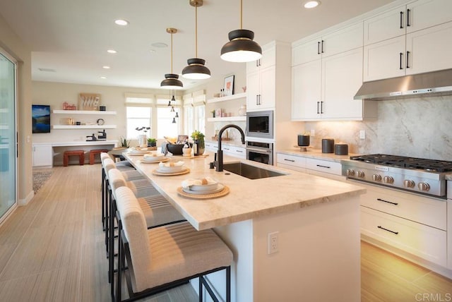 kitchen with sink, appliances with stainless steel finishes, an island with sink, a breakfast bar area, and light stone counters