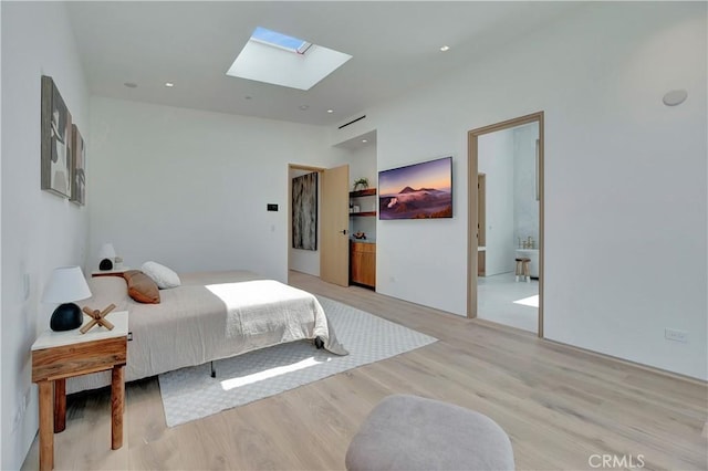 bedroom with light wood-type flooring, a skylight, and connected bathroom