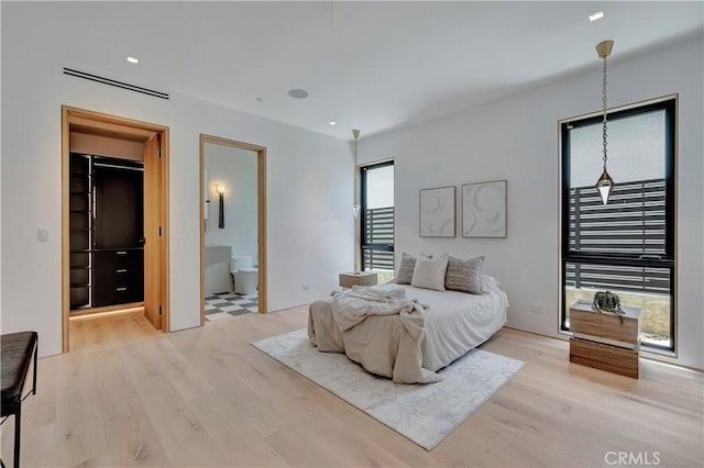 bedroom featuring ensuite bath, light wood-type flooring, and a spacious closet