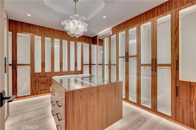 spacious closet with a chandelier, light hardwood / wood-style flooring, and a raised ceiling