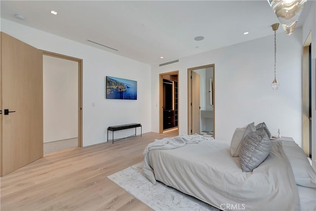 bedroom with ensuite bath, a spacious closet, and light hardwood / wood-style floors