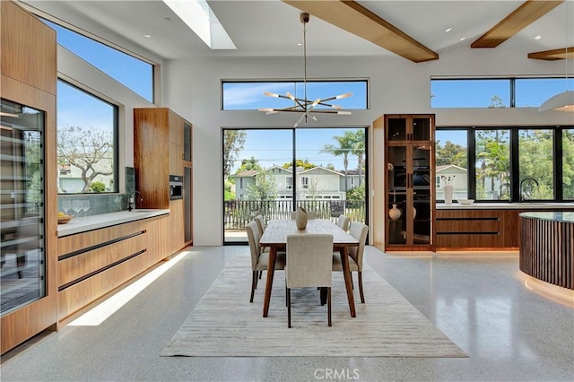 dining space featuring a healthy amount of sunlight, beam ceiling, a towering ceiling, and an inviting chandelier